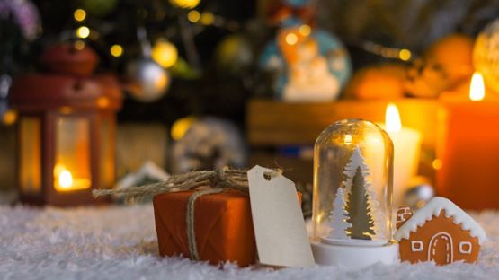 Orange gift, with tag, beside a snow globe and small toy house with candles and lanterns in the background.